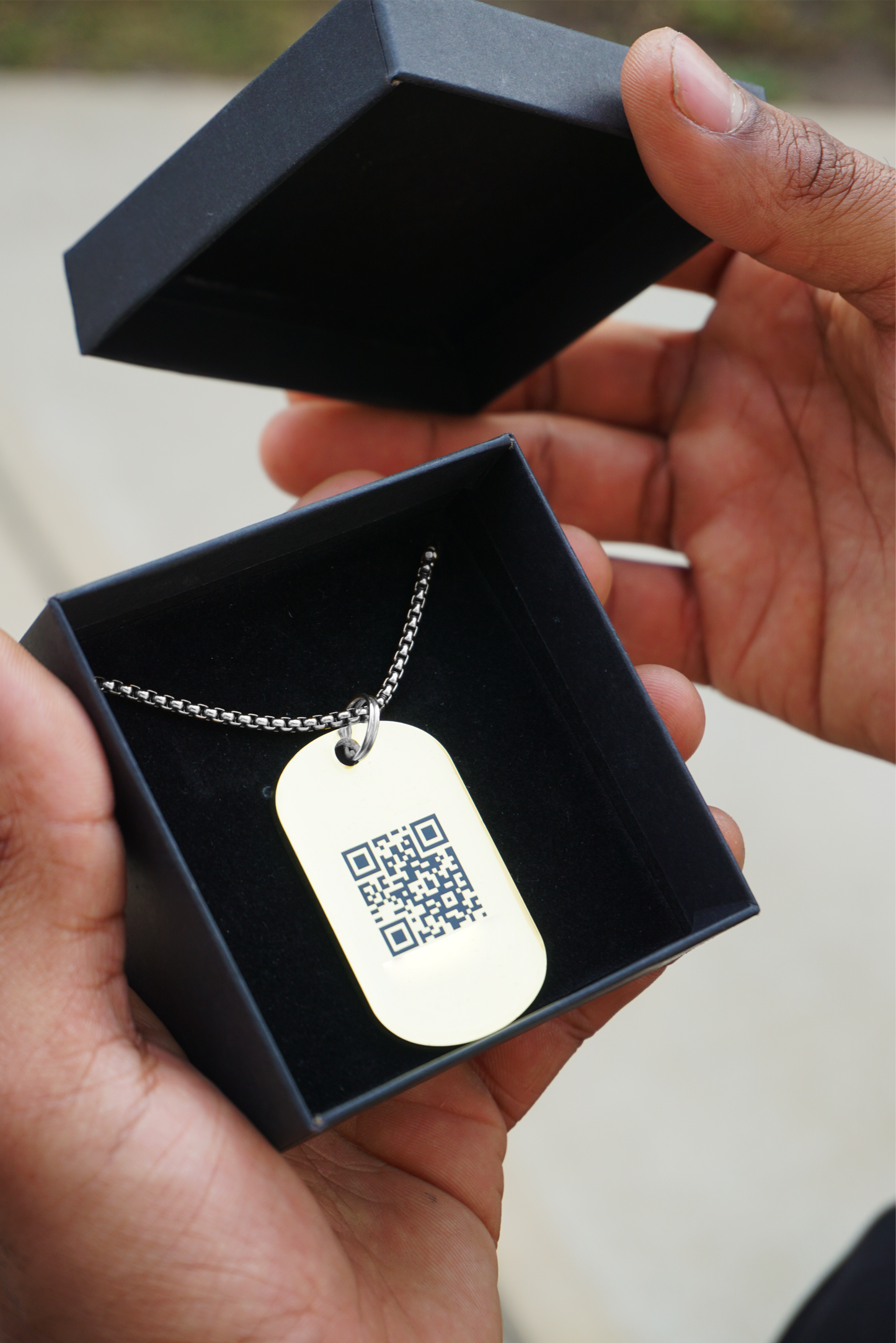 Hand opening a jewelry box to reveal a silver Jumptag wearable tech necklace with the Jumplink QR code facing up