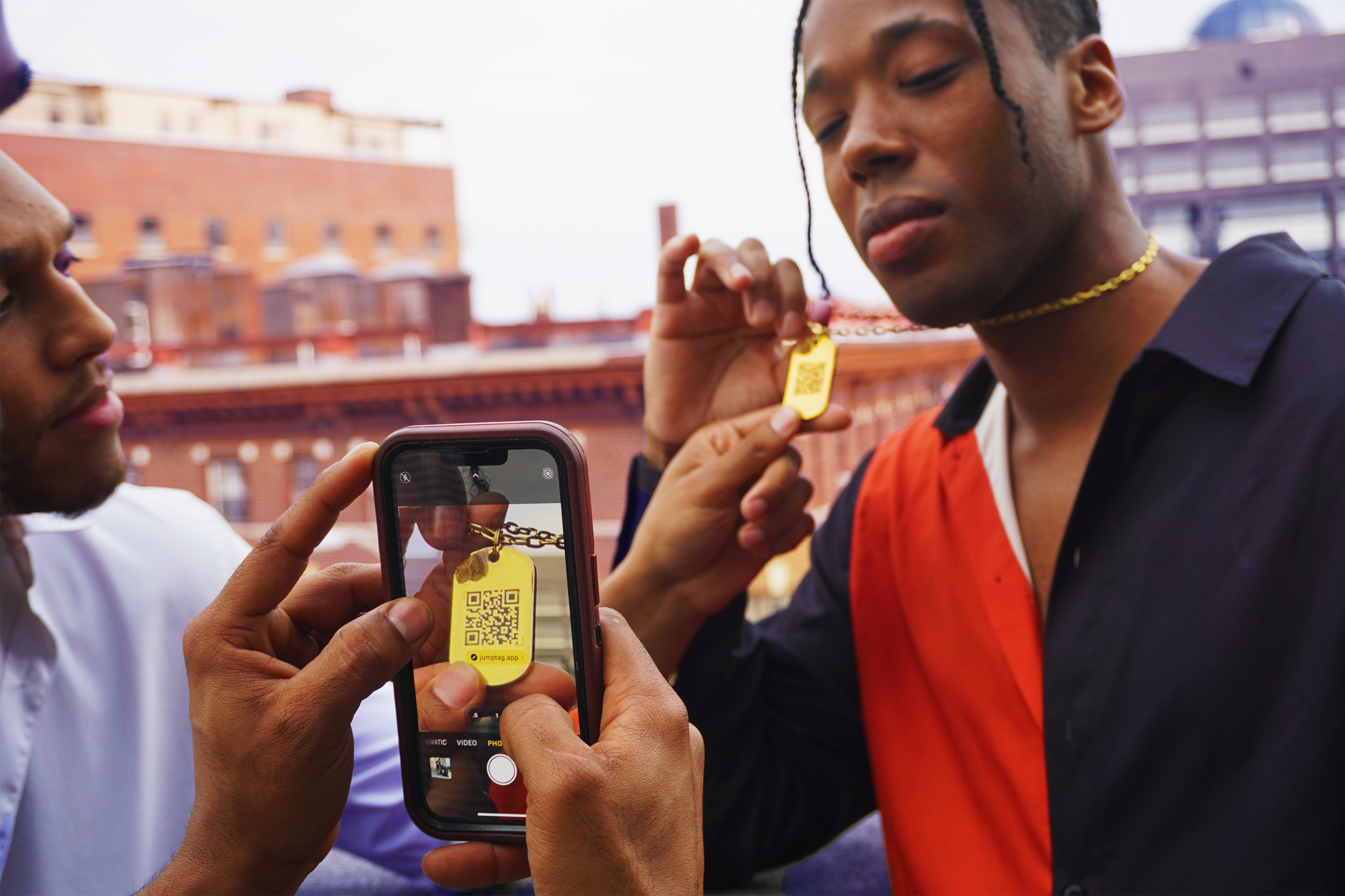 Shawn Red wearing a golden Jumptag QR necklace, a friend scans the dog tag with a phone's camera app & is visible on screen
